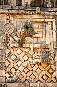 Uxmal - The Nunnery Quadrangle. The West building. Detail of the tail and the head of the two serpents of the facade; note the human head, wearing mask, within serpent's open jaws.