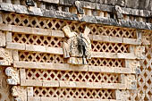 Uxmal - The Nunnery Quadrangle. The Eastern building. Frieze showing trapezoidal tiering of 8 double headed serpents bars, with small owl head at top against a latticework background.