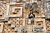 Uxmal - Palace of the Governor, front (East) facade. Frieze between 4th and 5th doorway from left representing a human figure with elaborate feathered headdress, seated on throne.