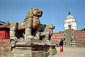 Bhaktapur - Durbar Square - two isolated lion statues are in the middle of the east end of the square, on the background the white sikkara of Fasidega temple. 