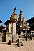 Bhaktapur - Durbar Square - Statue of Bhupatindra Malla King on top of a pillar, behind it the Taleju bell and the Vatsala Durga temple