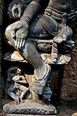 Hirapur - the Sixtyfour Yoginis Temple, weastern niche of the south wall of the mandapa, a ten armed figure with erected penis, with his leg he is pressing the head of a figure, in the pedestal a female attendant.