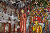 Dambulla cave temples - the narrow Cave 1, Devaraja Viharaya (Temple of the Lord of the Gods) statue of Ananda at the feet of the sleeping Buddha statue.